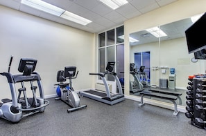 Academia com bicicletas ergométricas, esteiras e um banco de musculação.