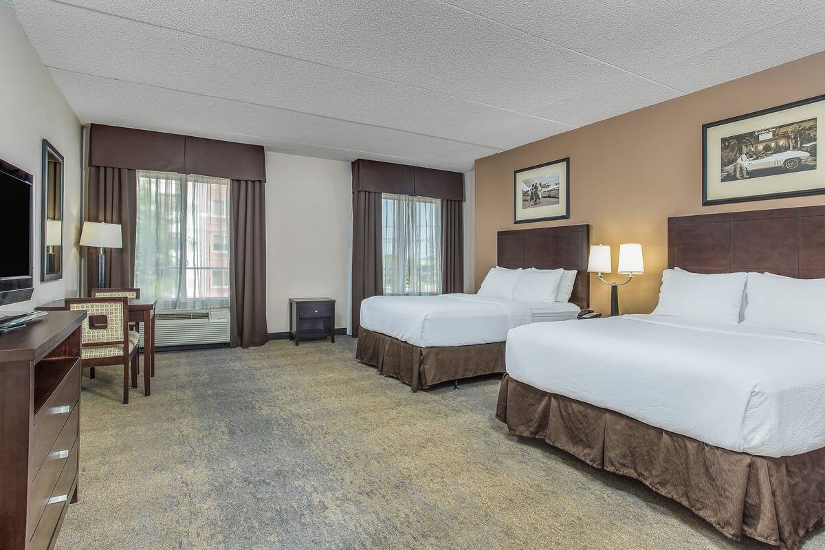 A hotel room with two beds, a desk, a chair, a TV, and a window with curtains.