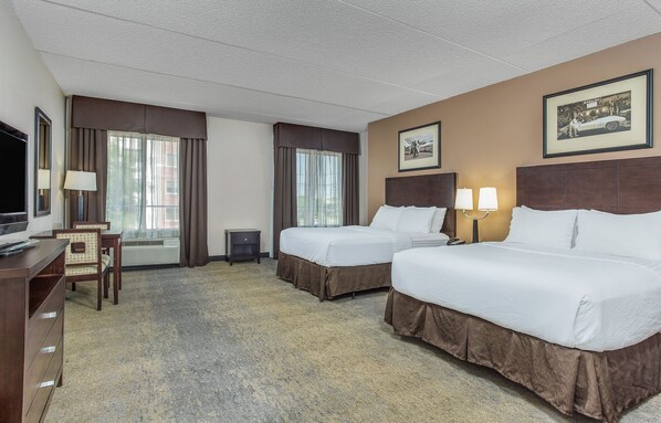 Quarto de hotel com duas camas, uma mesa, uma cadeira, uma televisão e uma janela com cortinas.