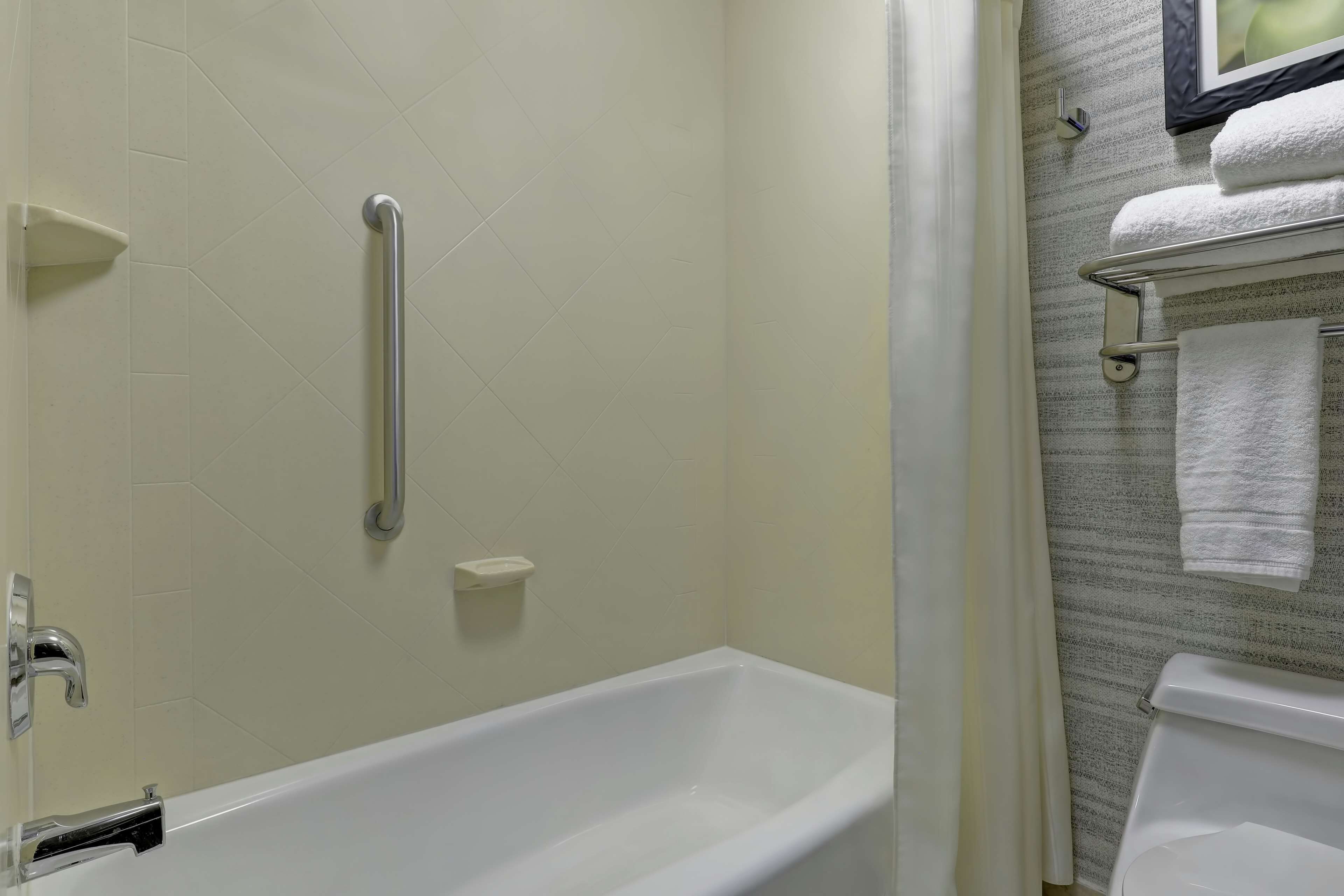 Un baño con una bañera blanca, un pasamanos, un perchero con toallas y un cortinón de ducha.