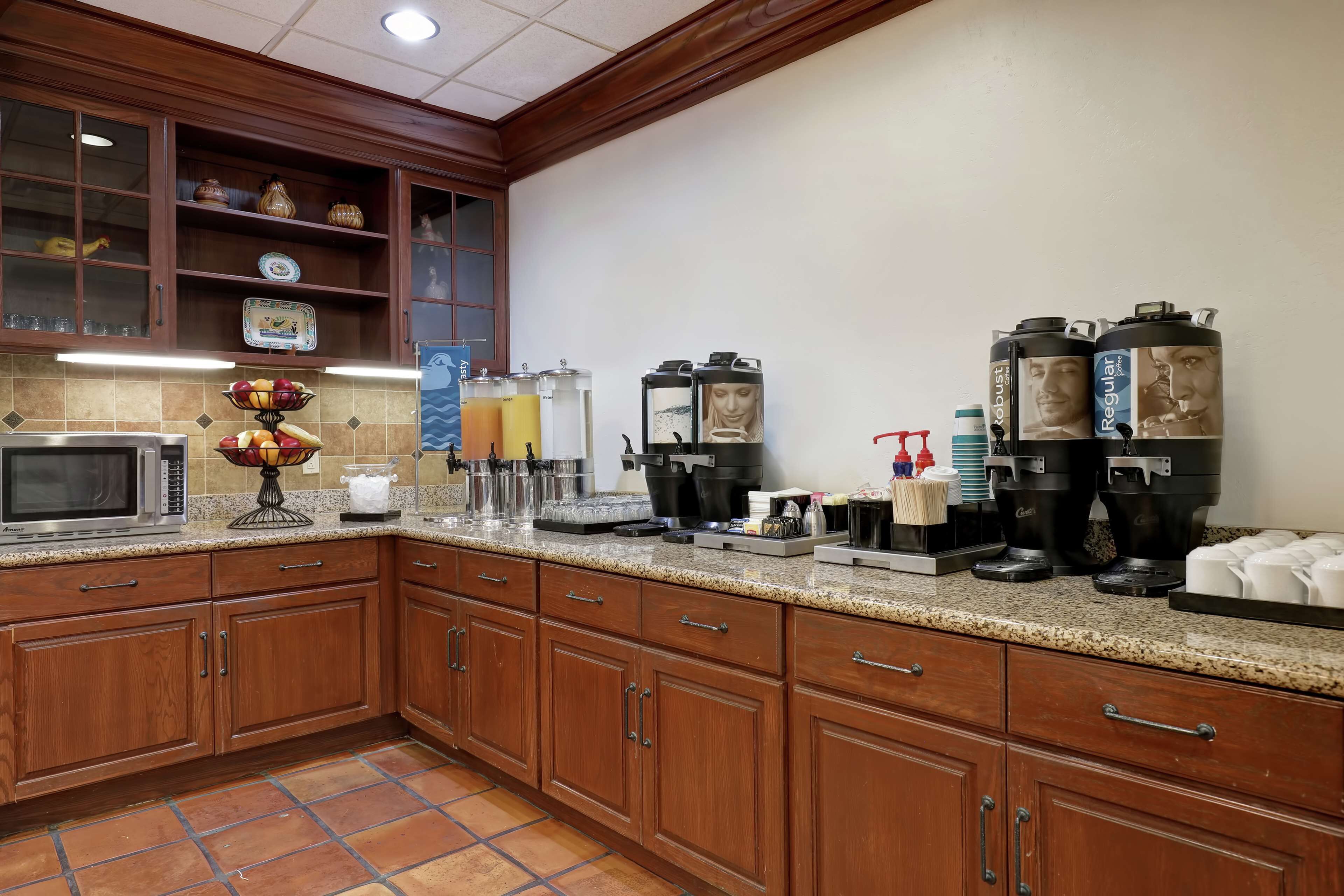 A kitchen with wooden cabinets, a microwave, a fruit bowl, and coffee makers.