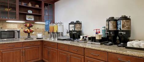 A kitchen with wooden cabinets, a microwave, a fruit bowl, and coffee makers.