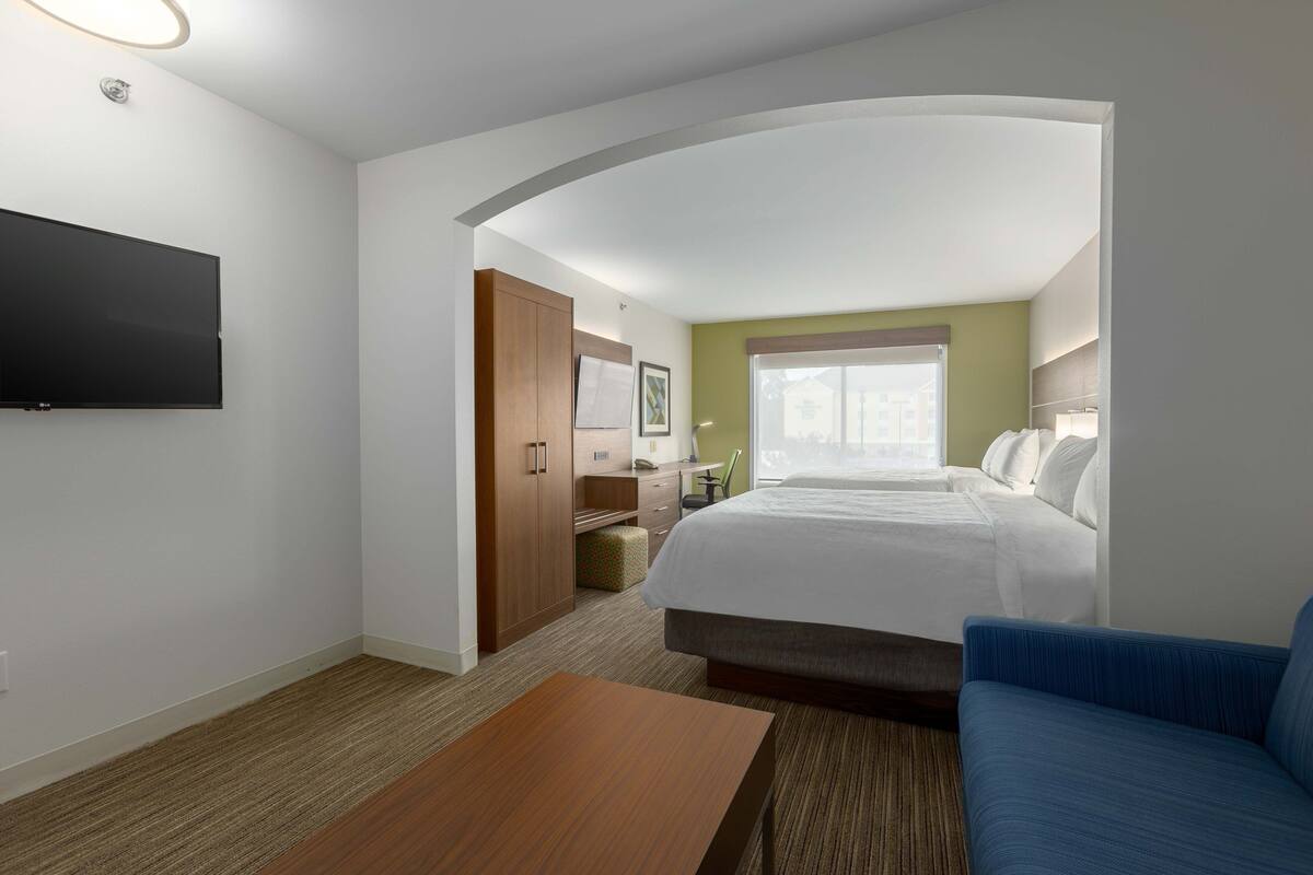 A hotel room with a bed, a TV mounted on the wall, a desk, and a window with a view.
