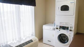 A laundry area with stacked washers and dryers, a vent, and a window with sheer curtains.