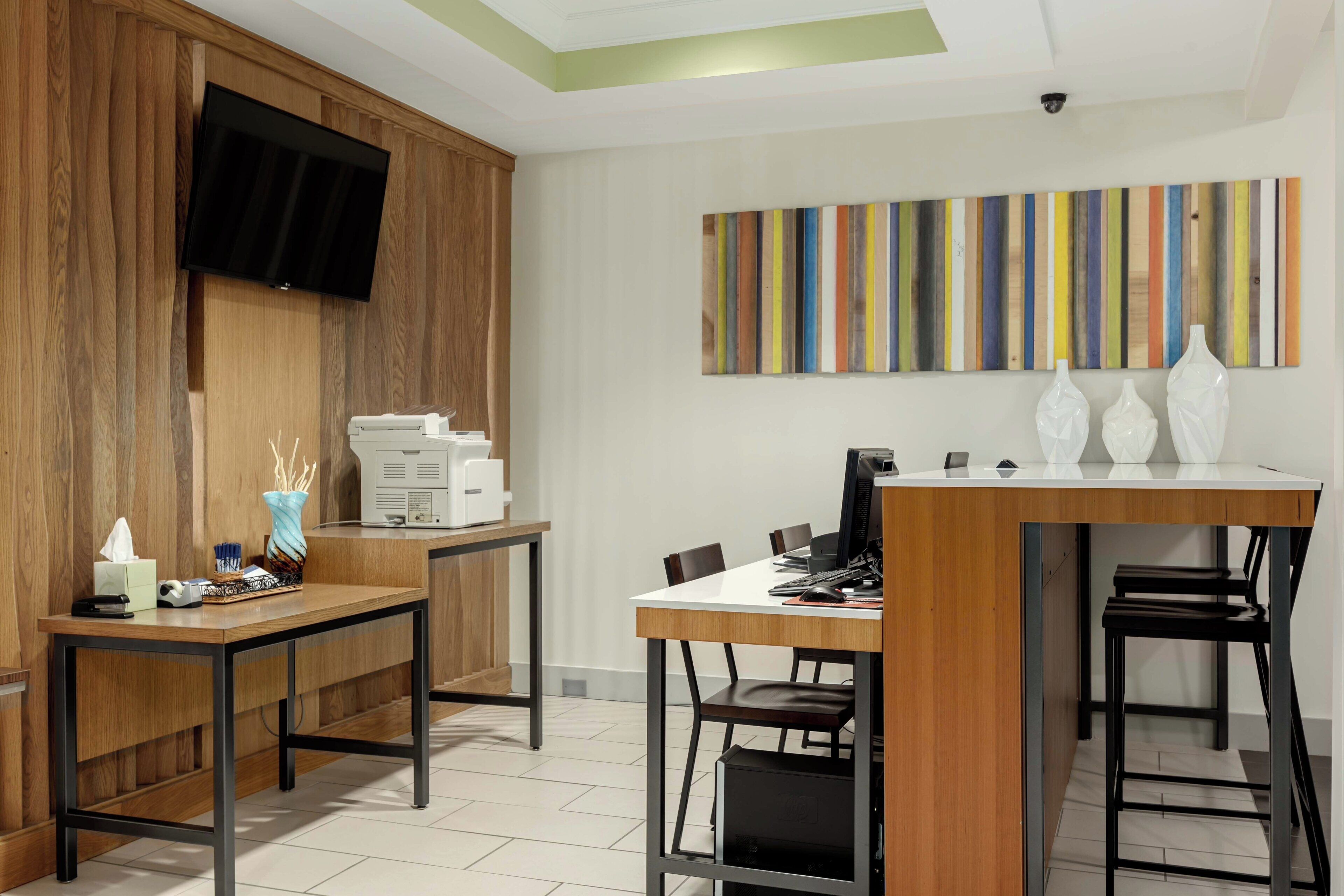 A modern office space with a wooden desk, a computer, and a flat-screen TV mounted on the wall.