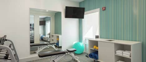 A gym with exercise equipment, a mirror, a television, and a shelf with towels.