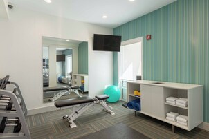Un gimnasio con equipo de ejercicio, un espejo, un televisor y un estante con toallas.