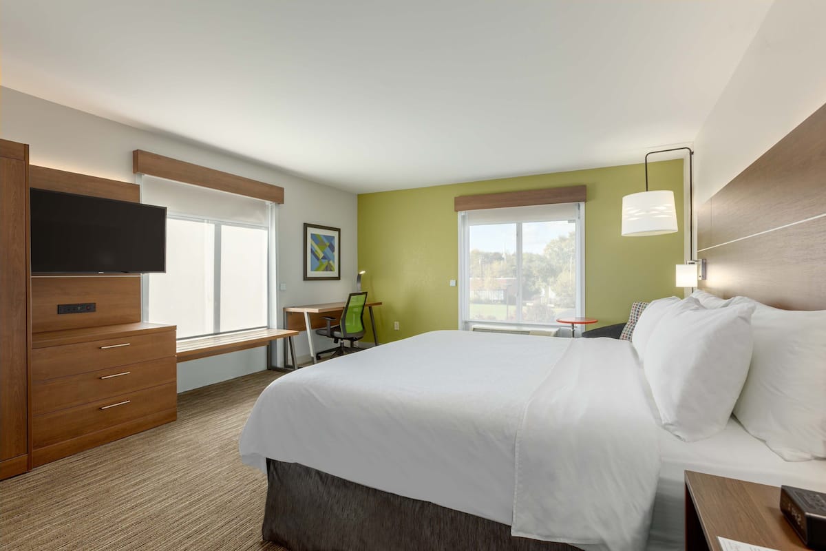 A hotel room with a large bed, a desk, a chair, a television, and a window with a view.