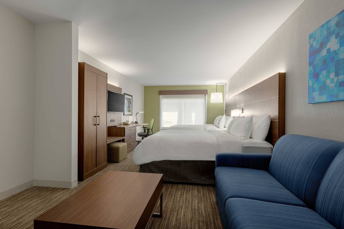 A hotel room with a bed, a blue sofa, a desk with a chair, a TV, and a window with curtains.