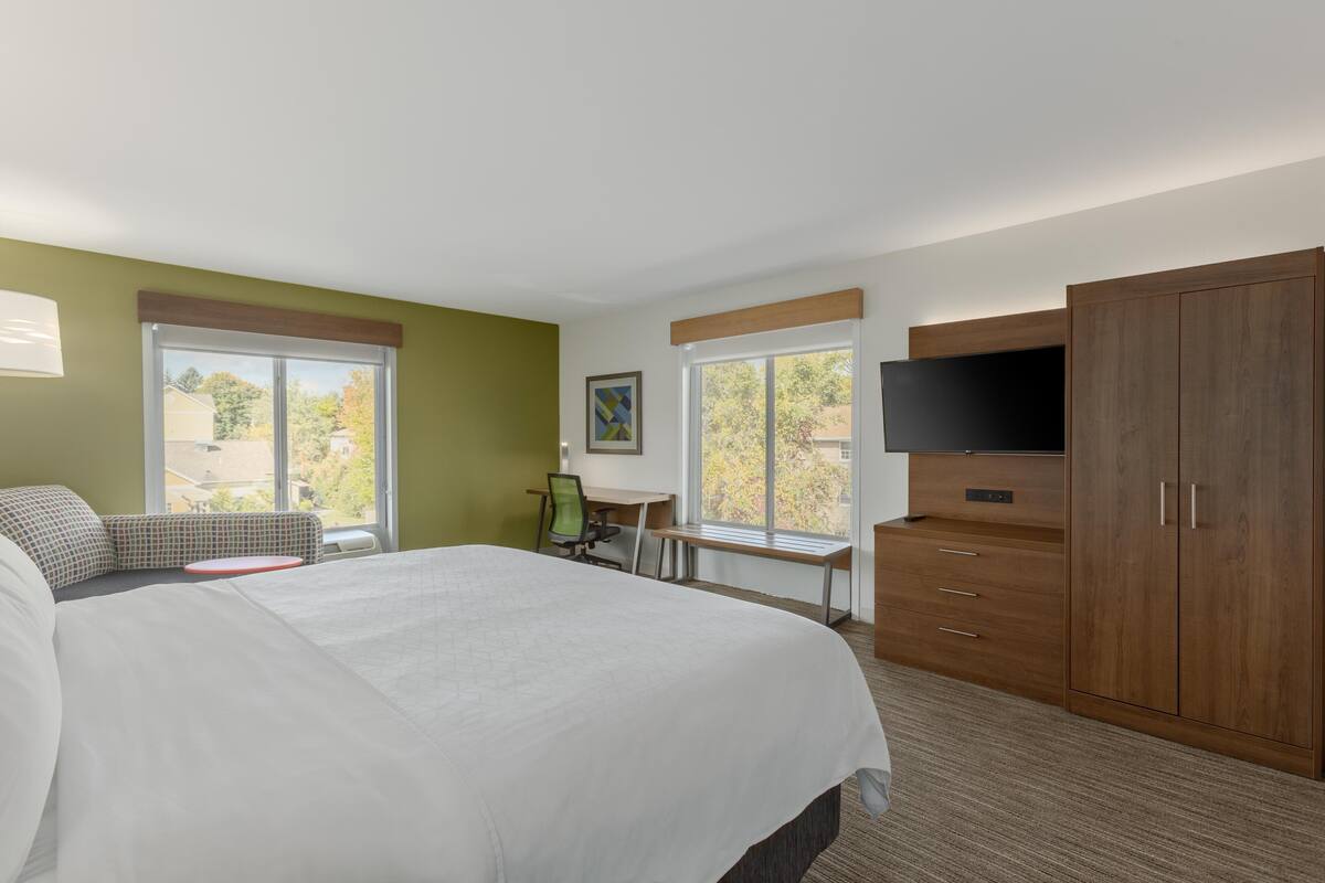 A hotel room with a large bed, a desk with a chair, a TV, and a wardrobe.