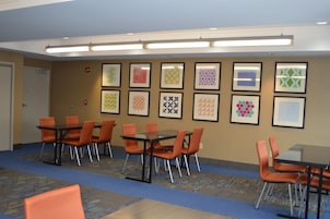 A conference room with tables and chairs, a patterned carpet, and framed artwork on the walls.