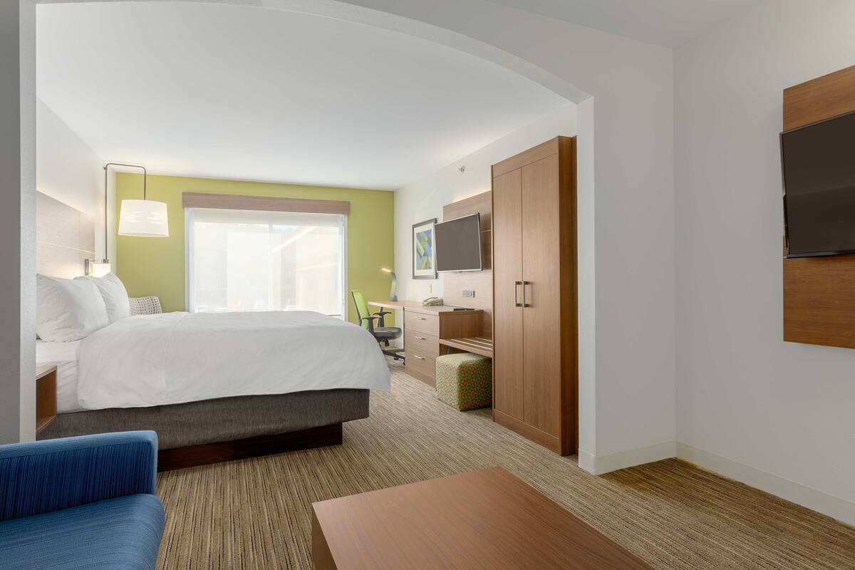 A hotel room with a bed, a desk, a chair, a TV, and a wardrobe.