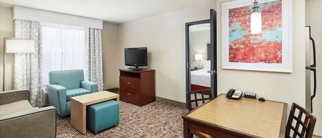 Une chambre d’hôtel avec un canapé, une petite table, un téléviseur, un bureau avec un téléphone et un grand tableau abstrait accroché au mur.