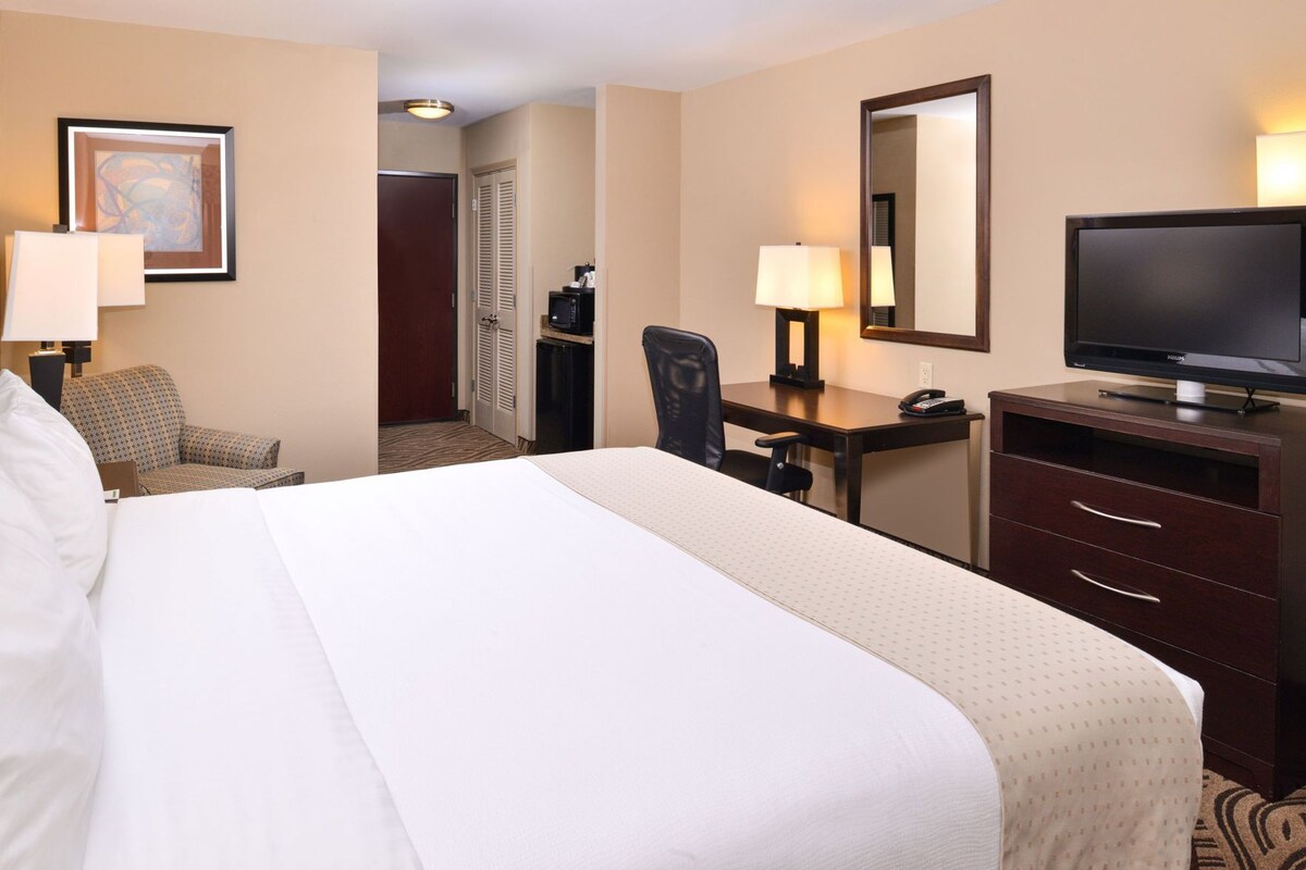 Ein Hotelzimmer mit einem großen Bett, einem Schreibtisch mit Stuhl, einem Fernseher und einer Schreibtischlampe.