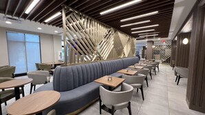 A modern restaurant interior with a curved seating area, wooden tables, and a unique geometric wall design.