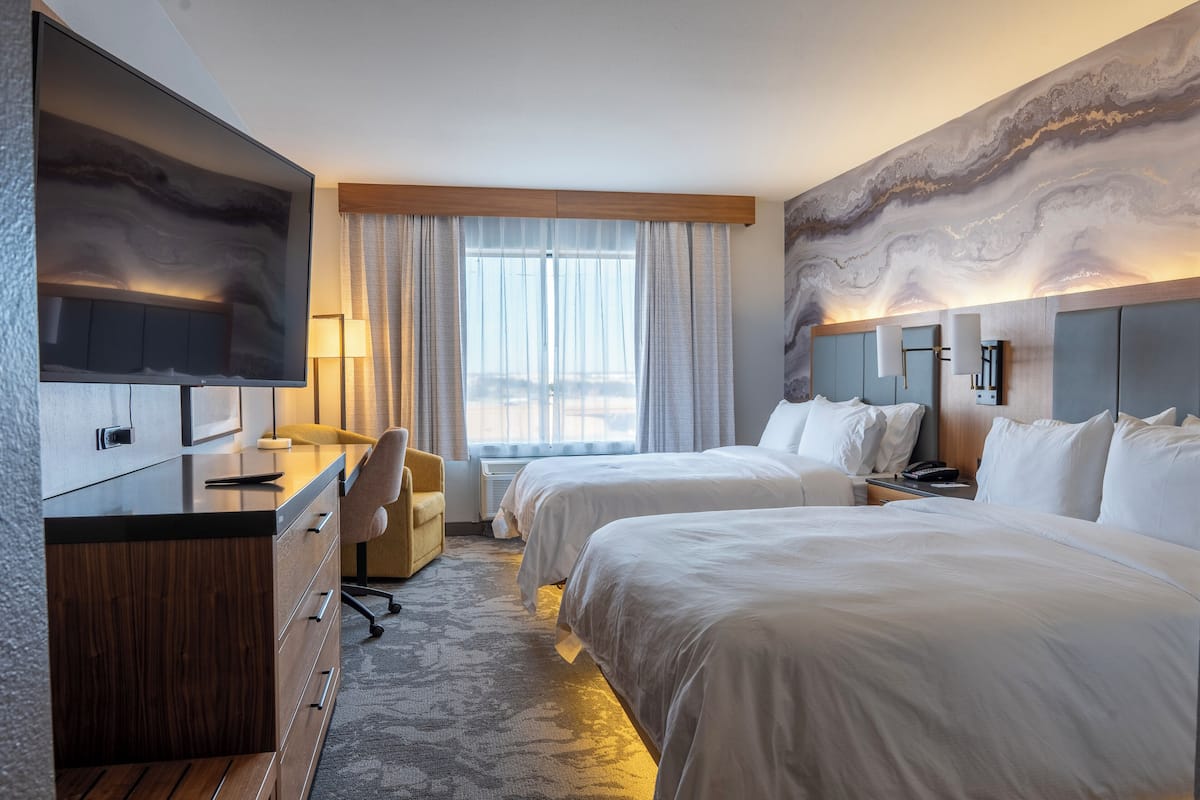 Une chambre d’hôtel avec deux lits, un bureau, une télévision et une grande fenêtre avec des rideaux.