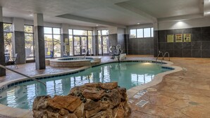 An indoor swimming pool with clear water, stone flooring, and safety signs on the walls.