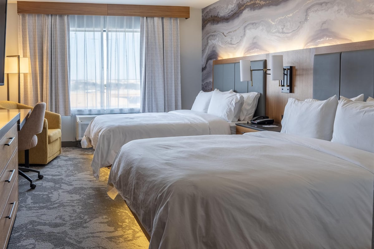 Une chambre d’hôtel avec deux lits, un bureau, une chaise, une lampe et une grande fresque abstraite sur le mur.