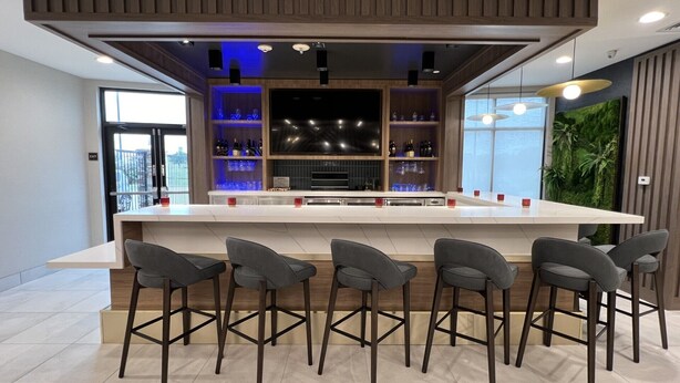 A modern bar area with a long counter, multiple stools, and a television screen.