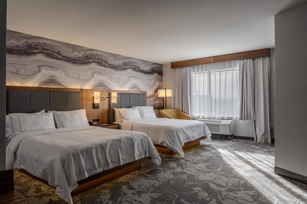 Une chambre d’hôtel avec deux lits, une grande fresque abstraite sur le mur, une fenêtre avec des rideaux et un sol recouvert de moquette.