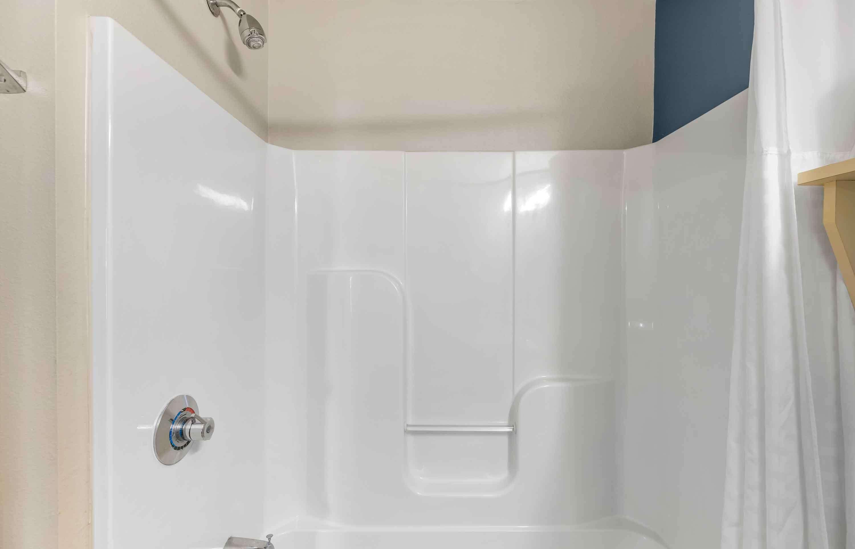 A white-tiled shower enclosure with a clear showerhead and a control knob.