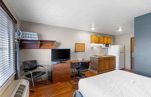 A compact hotel room with a bed, a desk with a computer, a TV, a kitchenette, and a window with blinds. - Extended Stay America Select Suites - Denver - Aurora (Aurora)