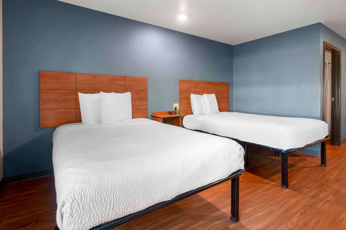 A hotel room with two beds, wooden headboards, and a blue wall.