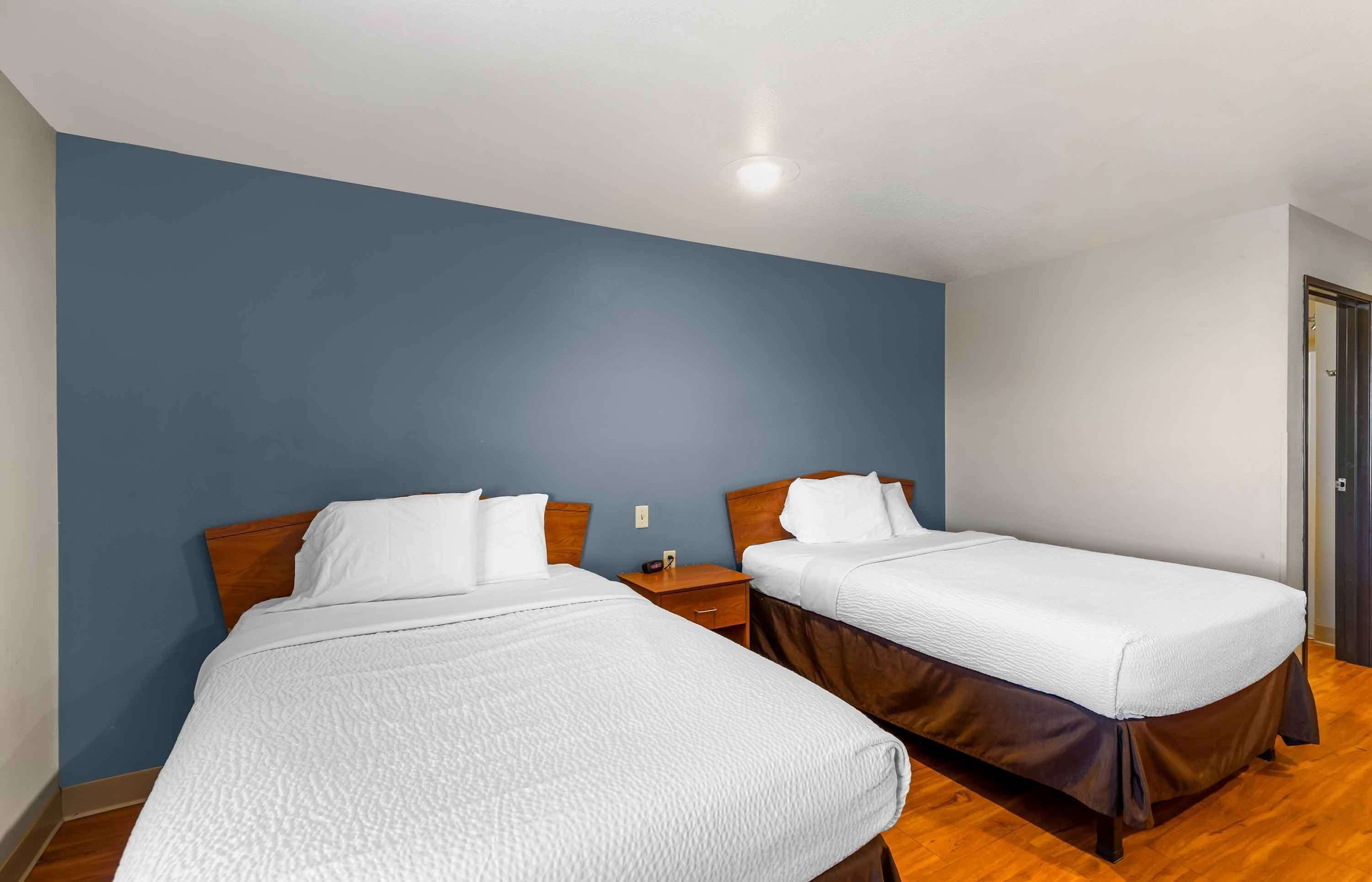 Habitació d'hotel amb dos llits individuals, amb caps de llit de fusta, roba de llit blanca, una tauleta de nit de fusta i una paret d'accent blava.
