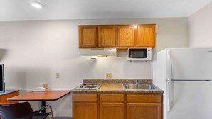 A compact kitchen with wooden cabinets, a microwave, a refrigerator, a stove, and a sink. - Extended Stay America Select Suites - Denver - Aurora (Aurora)