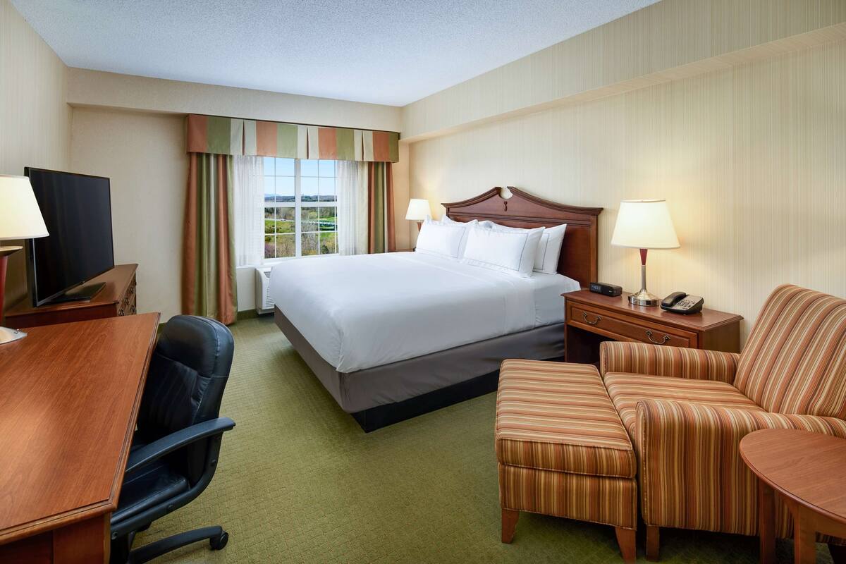 A hotel room with a bed, a desk, a chair, a sofa, and a TV.