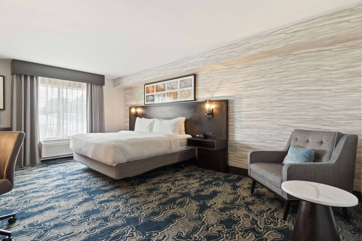 A hotel room with a large bed, a desk, a chair, and a small table.