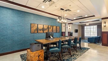 Una habitación de hotel con un escritorio de madera grande, varias sillas, un muro azul con textura y un candelabro.