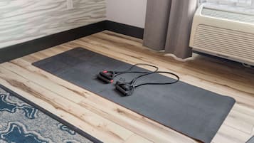 A yoga mat on a wooden floor with a power outlet and an air conditioner in the background.