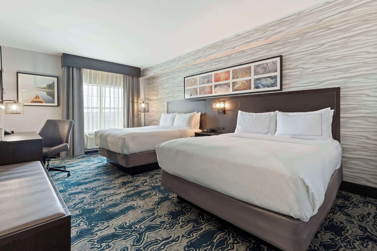 A hotel room with two beds, a desk, a chair, and a large window.