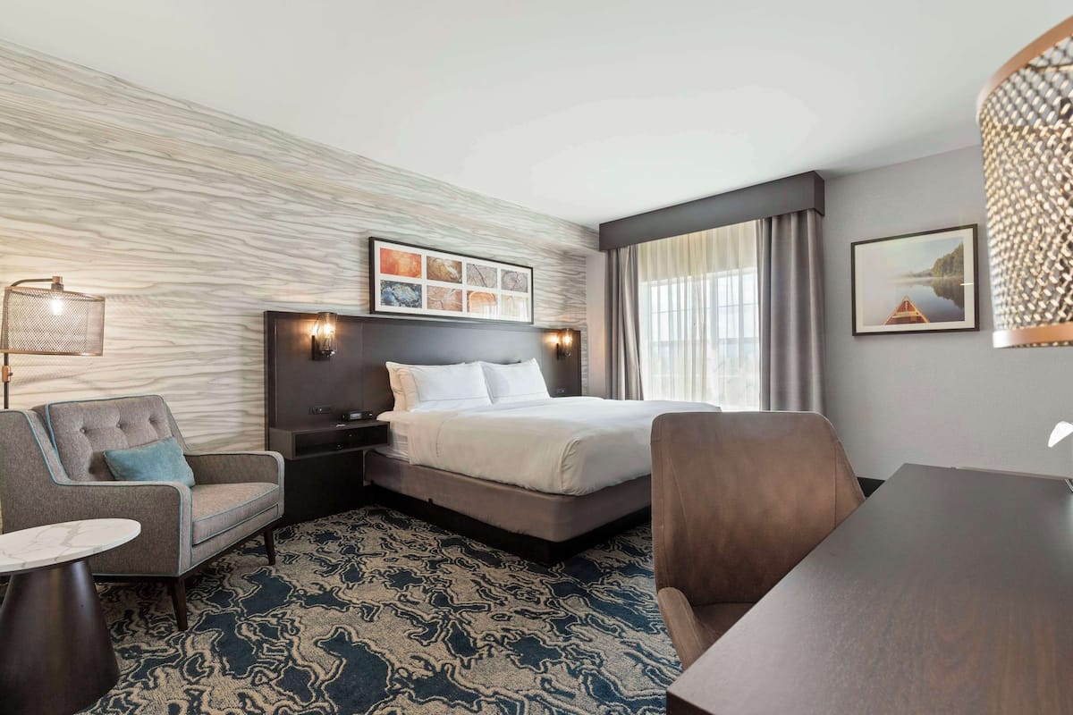A hotel room with a bed, a desk, a chair, a nightstand, and a lamp.