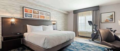 Ein Hotelzimmer mit einem großen Bett, einem Schreibtisch mit Stuhl, einem Laufband und einem großen Fenster mit Vorhängen.