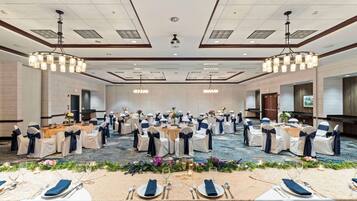 Une salle de banquet avec des tables rondes, des chaises blanches et bleu marine, et des centres de table floraux.