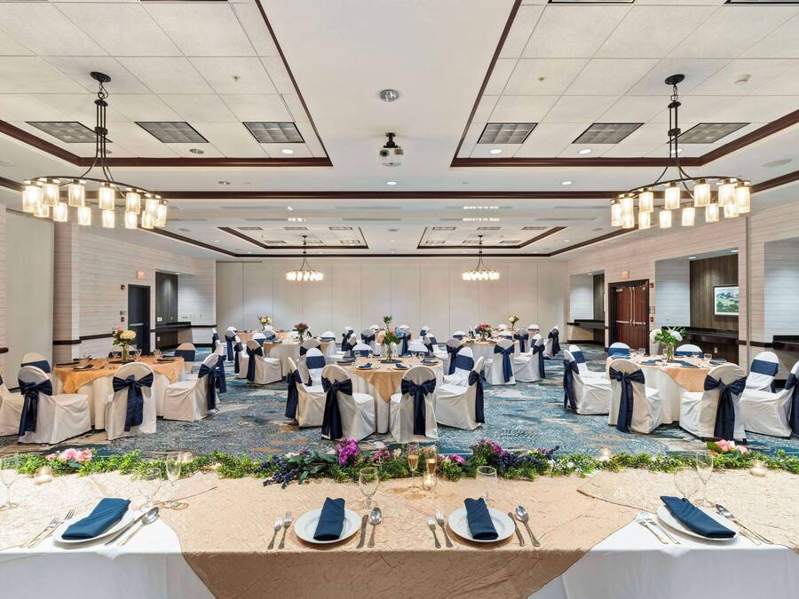 Une salle de banquet avec des tables rondes, des chaises blanches et bleu marine, et des centres de table floraux.