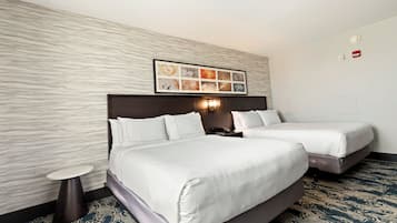 A hotel room with two beds, a small round table, a wall-mounted artwork, and a patterned carpet.