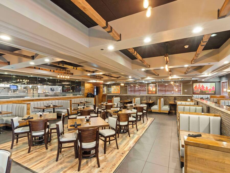 Un restaurante espacioso con techos altos, vigas de madera y diversas opciones de asientos, incluyendo cabinas y mesas.