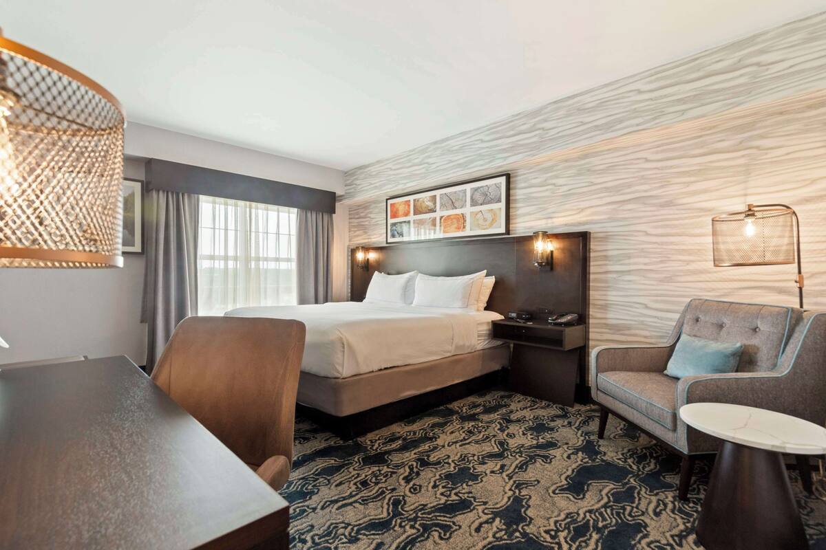 A hotel room with a bed, a desk, a chair, a small table, and a patterned carpet.