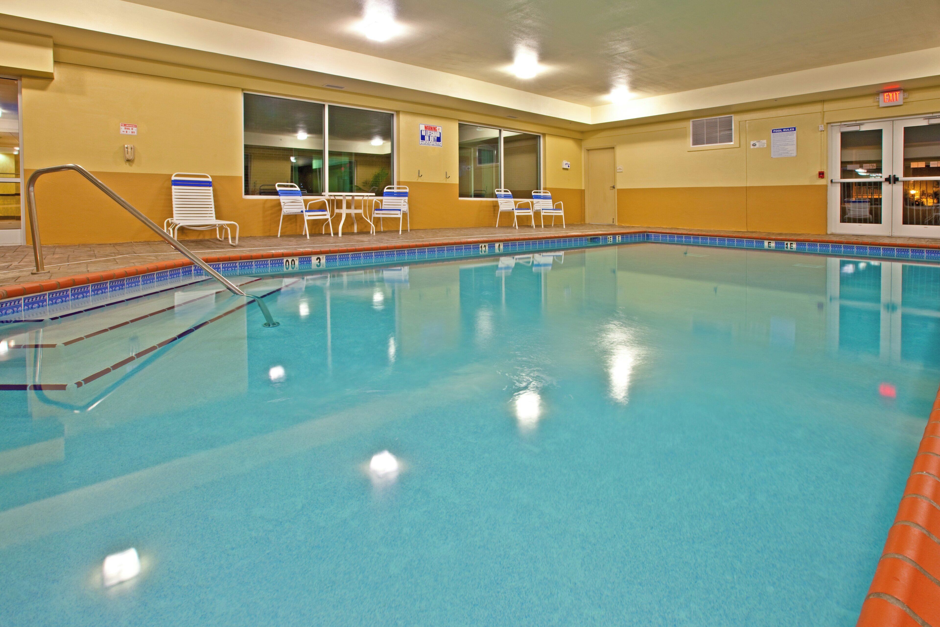 Una piscina interior con agua cristalina, un trampolín y varias sillas de descanso.