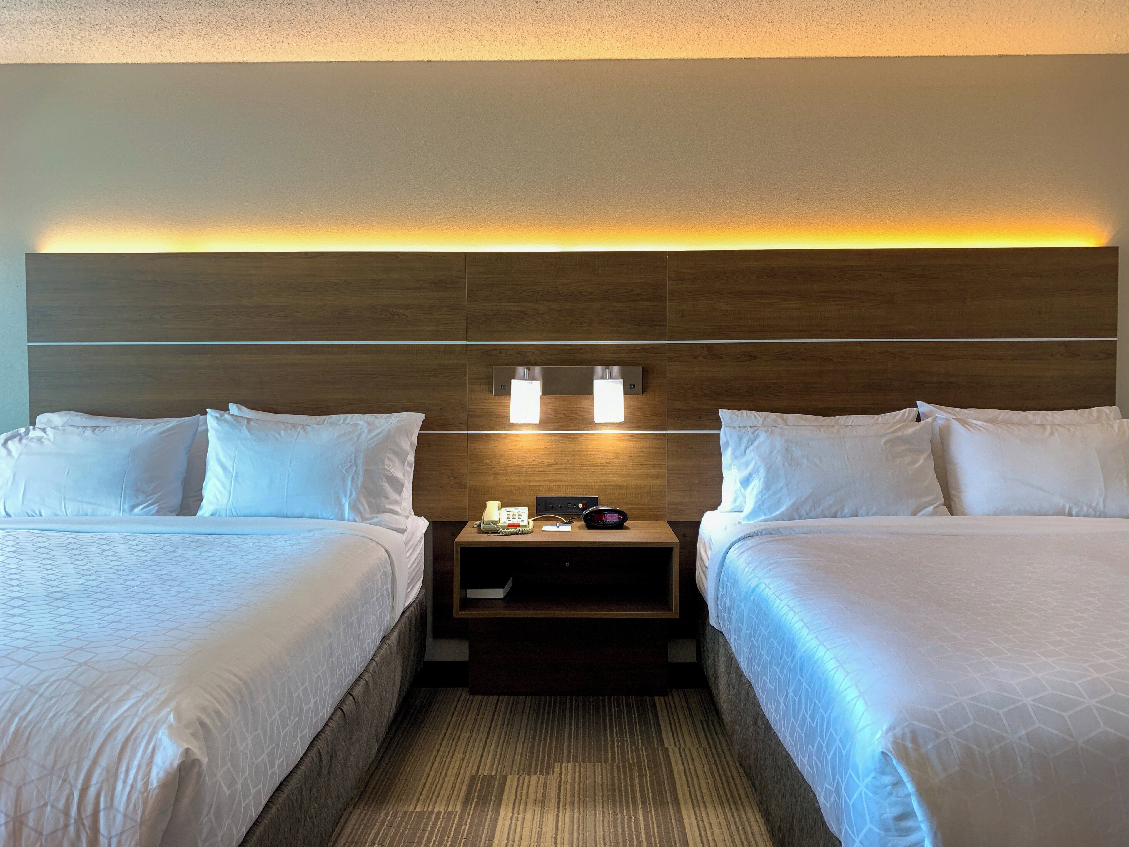 A hotel room with two beds, a nightstand, a phone, and a wall-mounted light fixture.