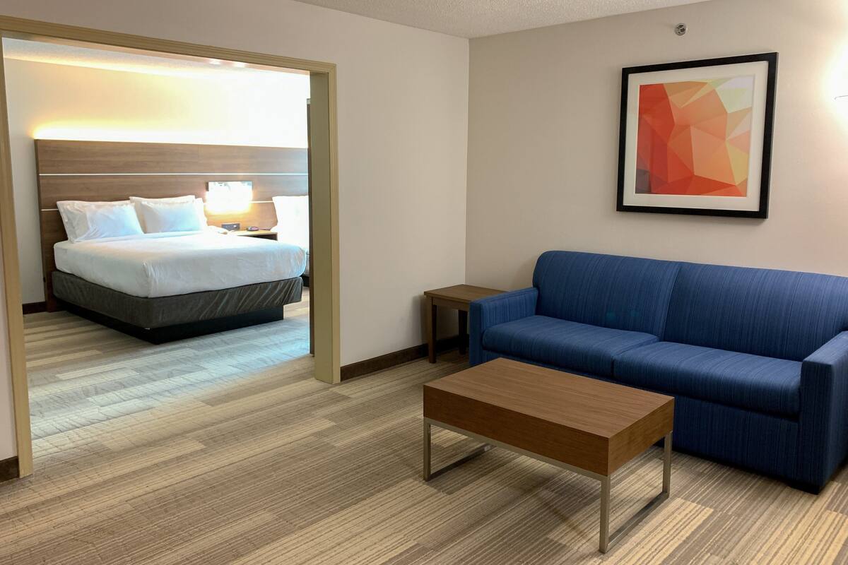 A hotel room with a bed, a blue sofa, a coffee table, and a framed abstract painting on the wall.