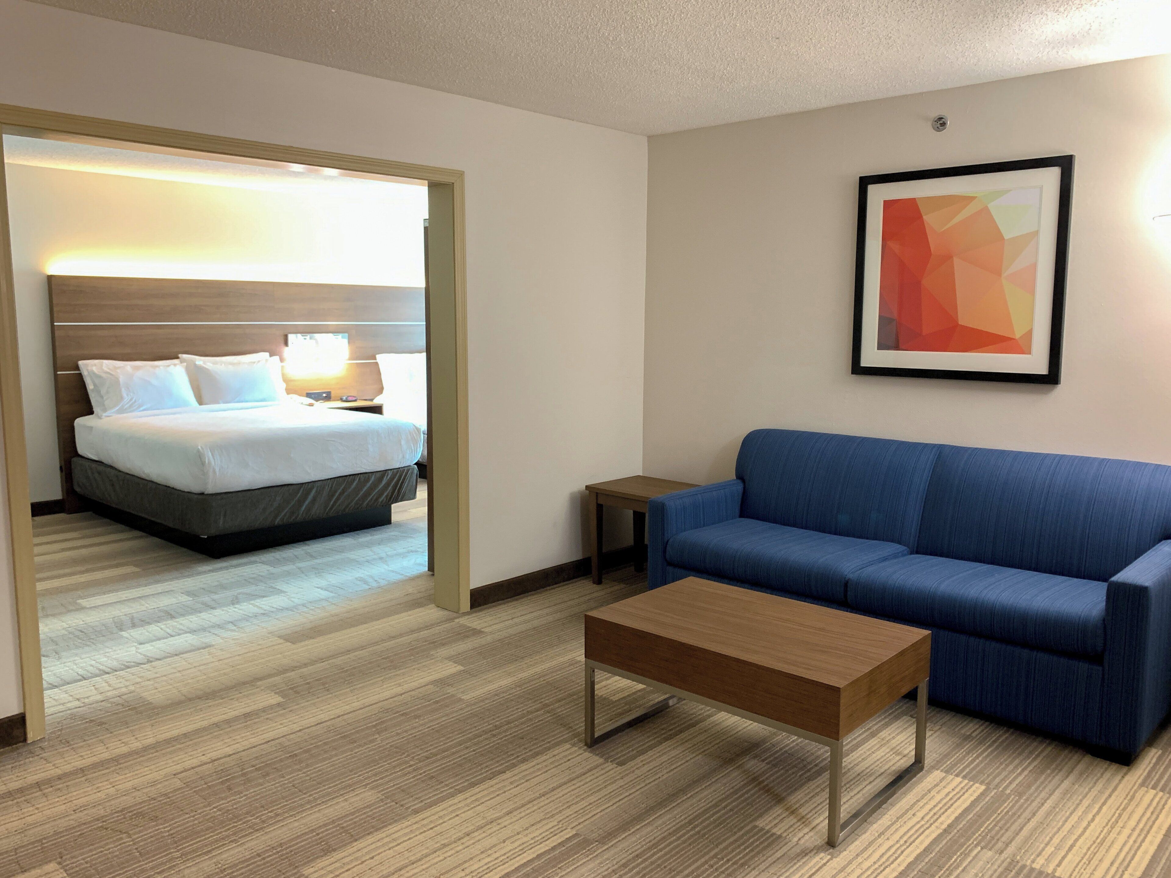 A hotel room with a bed, a blue sofa, a coffee table, and a framed picture on the wall.