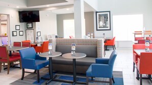 A modern hotel lobby with seating areas, a flat-screen TV, framed pictures, and a large window.