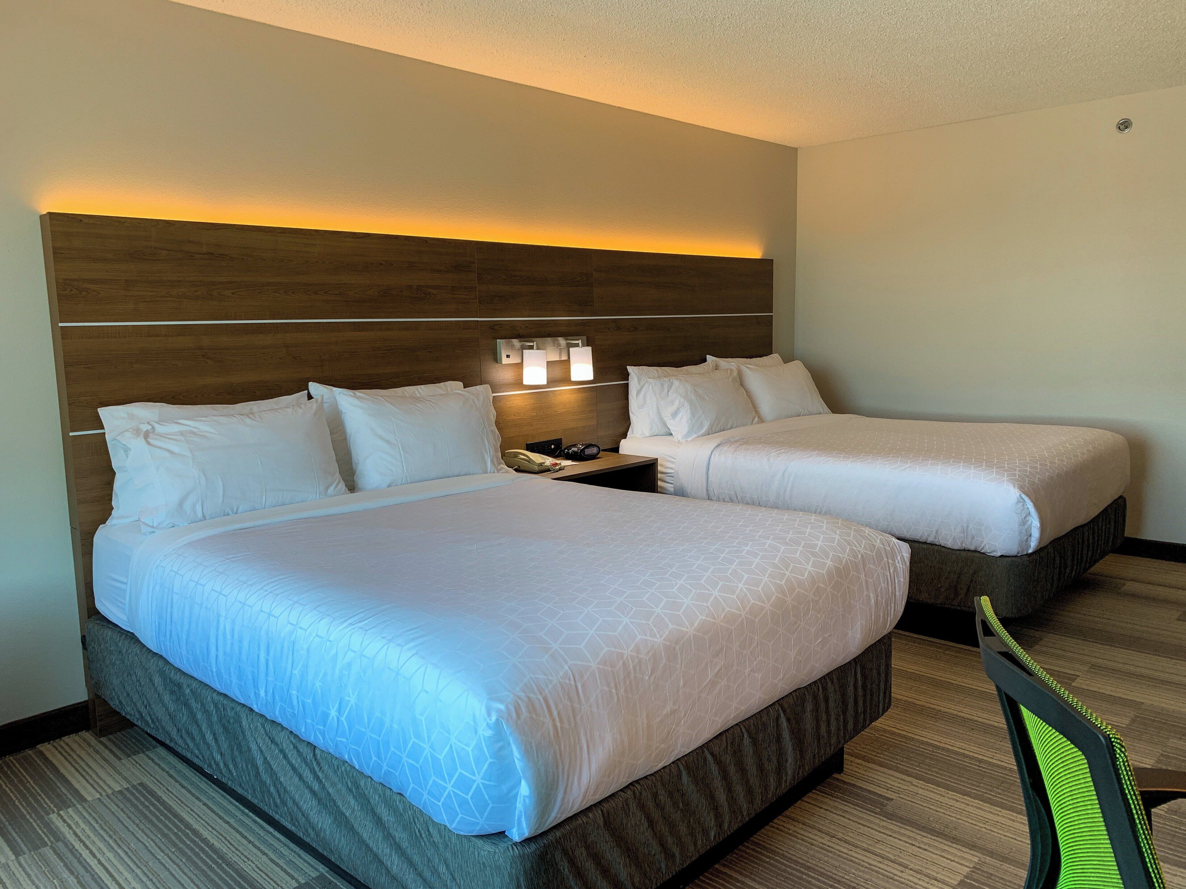 A hotel room with two beds, a wooden headboard, a nightstand with a phone, and a wall-mounted light fixture.