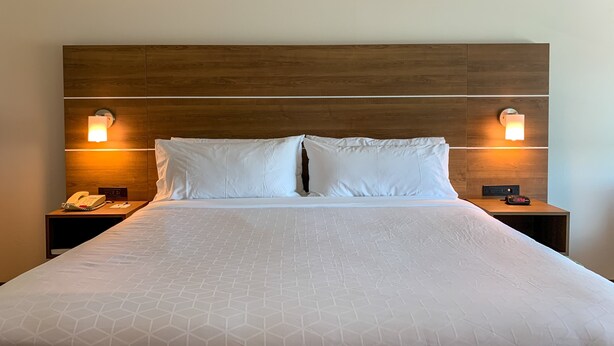 A hotel room with a wooden headboard, two bedside lamps, a telephone, and a digital clock on the nightstand.