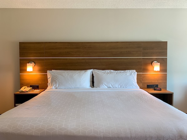Quarto de hotel com cabeceira de madeira, duas luminárias de apoio, telefone e relógio digital no criado-mudo.