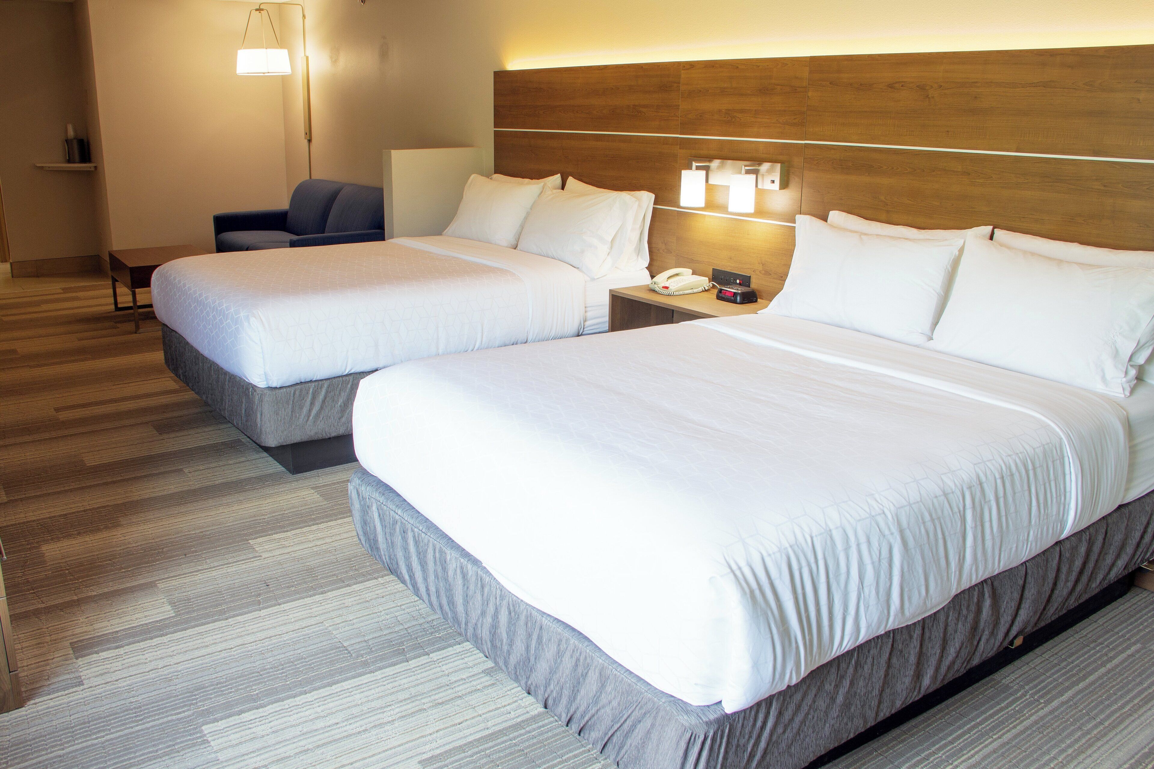 A hotel room with two beds, a bedside table with a phone, a lamp, and a chair.